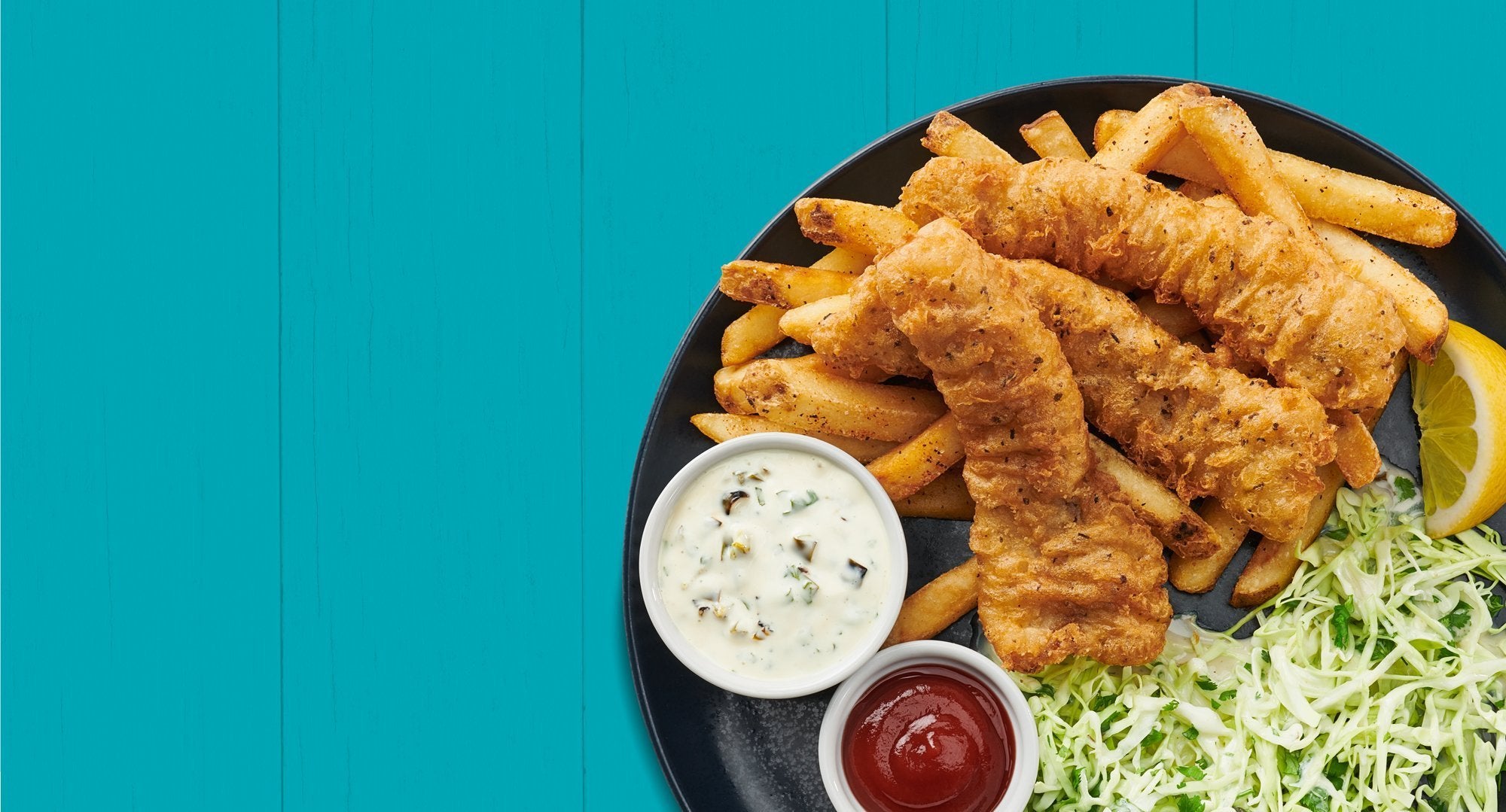 Fish and chips on a plate with sauces and a lemon wedge.