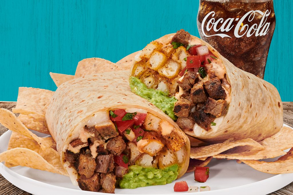 Two burritos on a white plate with tortilla chips and a glass of Coca-Cola.