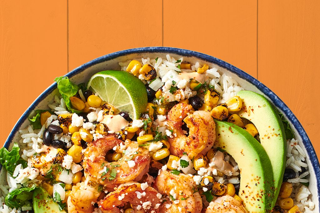 Shrimp bowl with rice, corn, black beans, cheese, avocado, and lime.