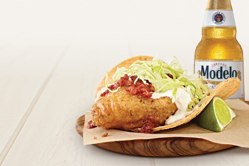 A fish taco with a bottle of Modelo beer and a lime wedge.